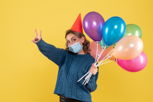 young female holding colorful balloons in mask on yellow