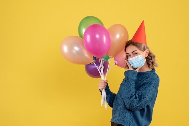 Giovane donna in possesso di palloncini colorati in maschera sul giallo