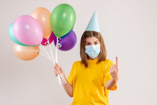 young female holding colorful balloons in sterile mask on white