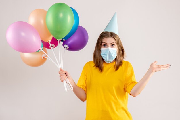 young female holding colorful balloons in sterile mask on white