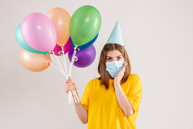 young female holding colorful balloons in sterile mask on white