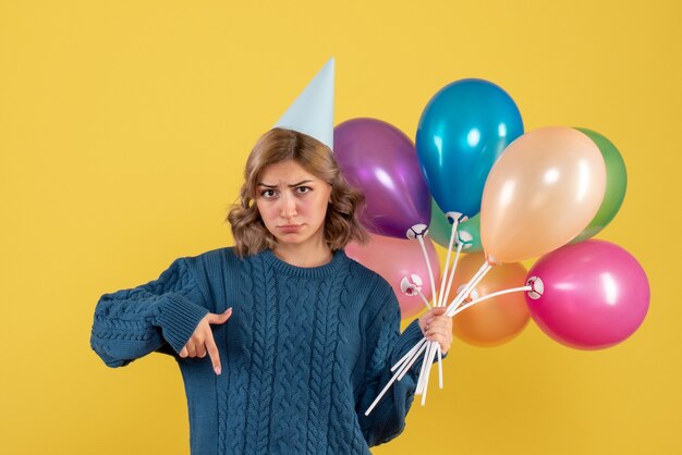 young female holding colorful balloons on yellow