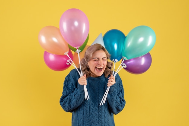 young female holding colorful balloons on yellow