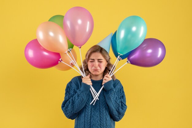 young female holding colorful balloons on yellow