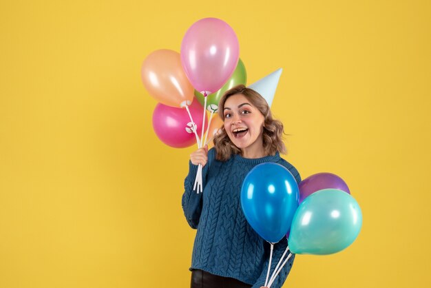 young female holding colorful balloons on yellow