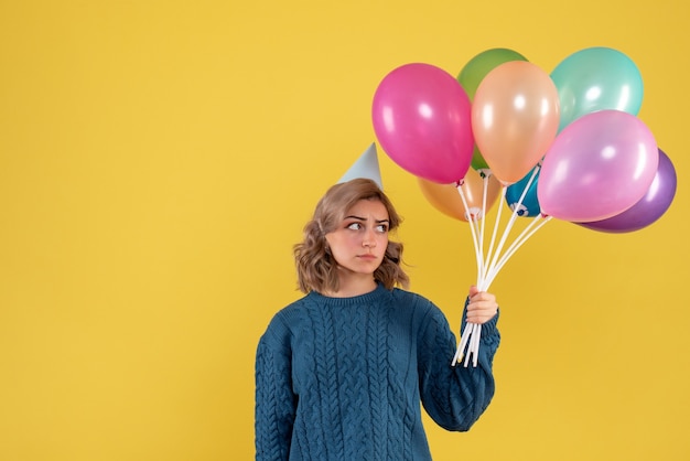 молодая женщина держит разноцветные воздушные шары на желтом