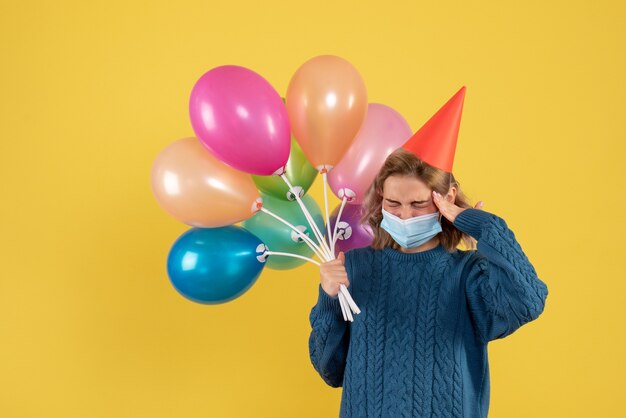 young female holding colorful balloons on yellow