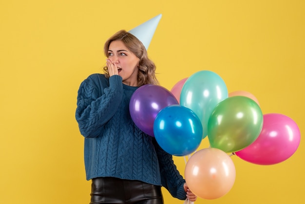 young female holding colorful balloons on yellow