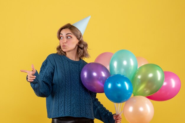 young female holding colorful balloons on yellow