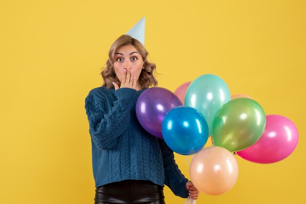 young female holding colorful balloons on yellow