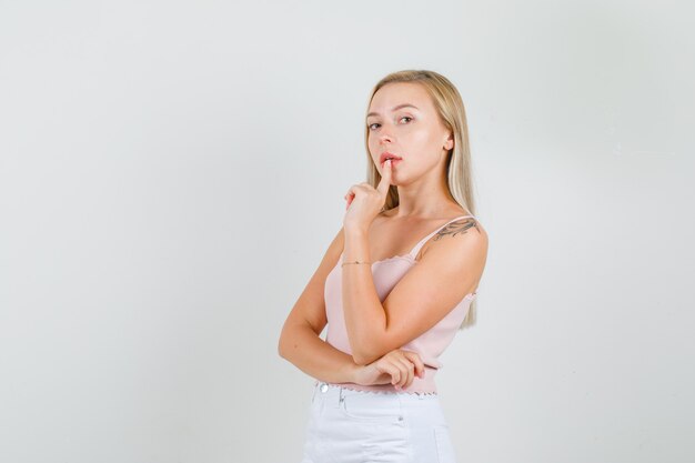 Young female holding finger on lip in singlet, mini skirt and looking confident