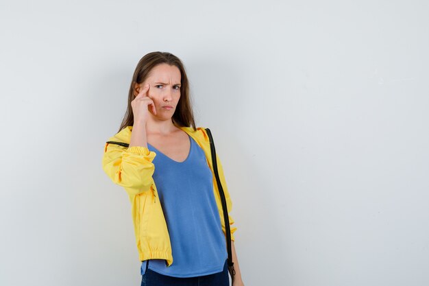 Young female holding finger on temples in t-shirt and looking intelligent. front view.