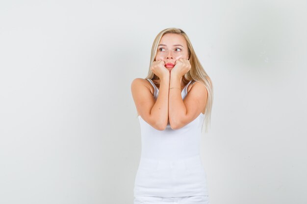 Young female holding fists on cheeks in white singlet