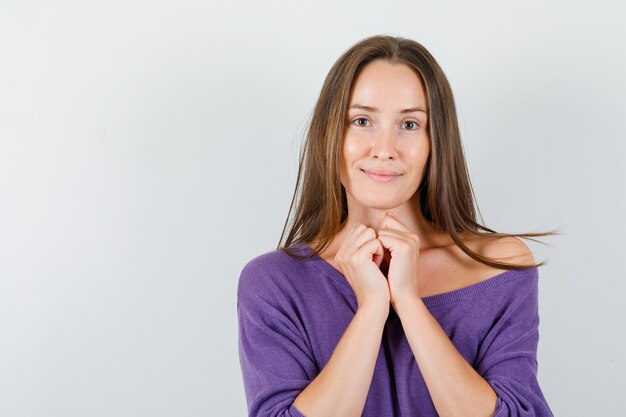 Young female holding folded hands together in violet shirt and looking beloved. front view.