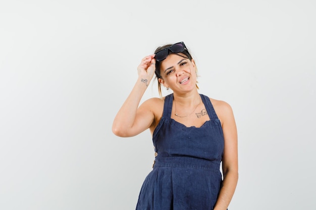 Young female holding glasses on head in dark blue dress and looking lovely