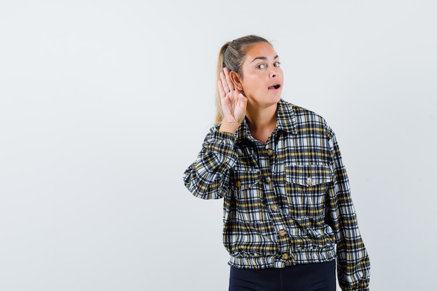 Free photo young female holding hand behind ear in shirt, shorts and looking curious , front view.