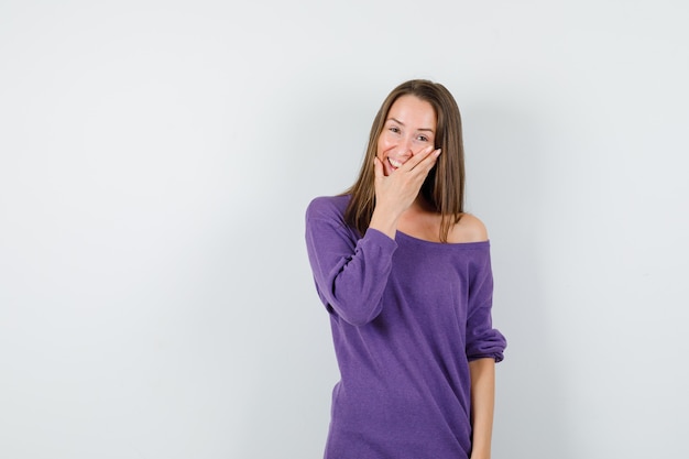 Young female holding hand on face in violet shirt and looking happy. front view.