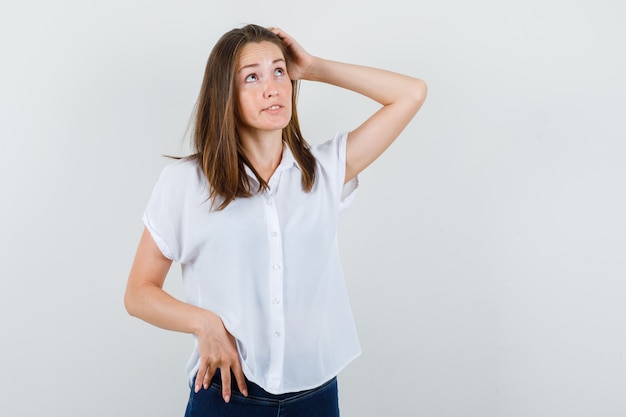 Young female holding hand on face in white blouse and looking pensive