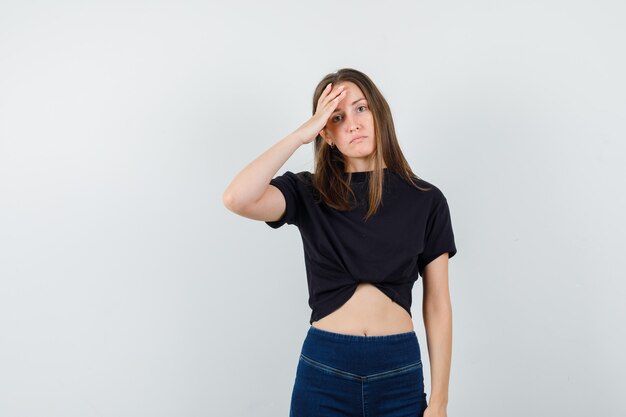 Young female holding hand on forehead in black blouse, pants and looking pensive