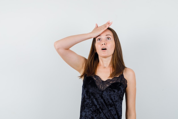 Young female holding hand on forehead in black singlet and looking wondered