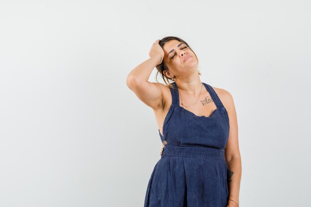 Young female holding hand on head in dark blue dress and looking fatigued