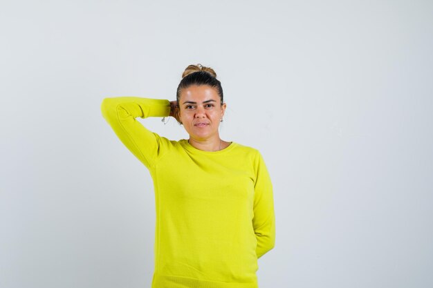 Young female holding hand behind head in sweater and looking charming