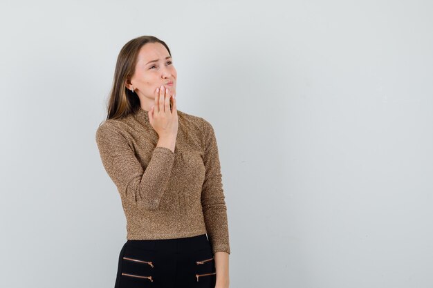 Young female holding hand on her chin in blouse,skirt and looking painful , front view. space for text