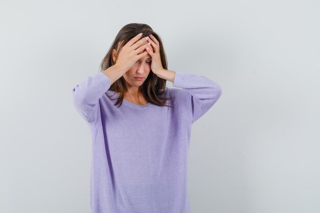 Young female holding hand on her forehead in lilac blouse and looking tangled 