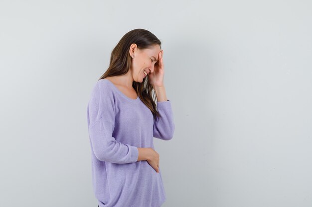 Young female holding hand on her forehead in lilac blouse .