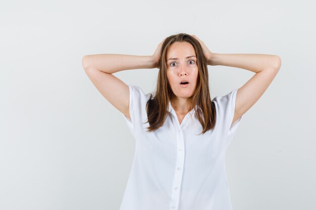 Young female holding hand on her head in white blouse and looking agitated