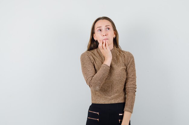 Young female holding hand on her mouth in blouse,skirt and looking troubled. front view. space for text