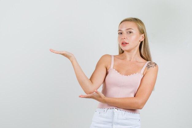 Young female holding hand like showing something in singlet