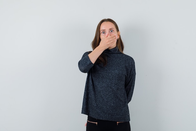 Young female holding hand on mouth in black blouse and looking scared. front view.