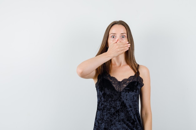 Young female holding hand on mouth in black singlet and looking scared