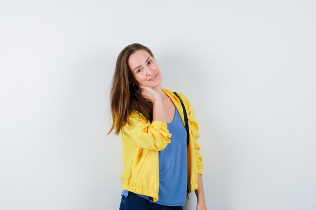 Young female holding hand on neck in t-shirt, jacket and looking attractive , front view.