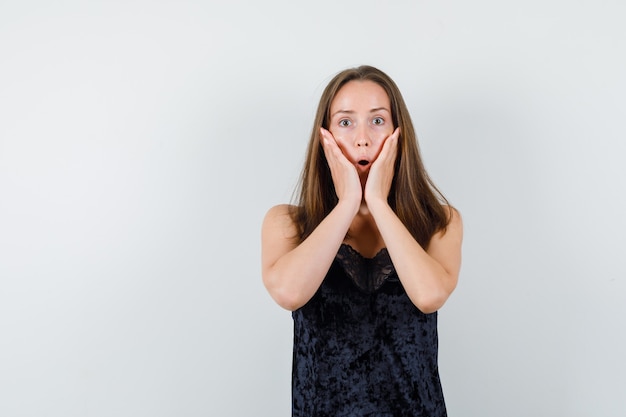 Young female holding hands on cheeks in black singlet and looking surprised