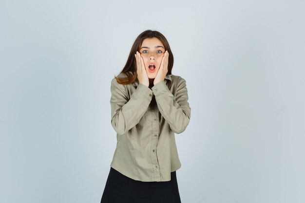 Young female holding hands on cheeks in shirt and looking shocked