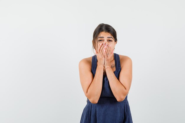 Young female holding hands on face in dark blue dress and looking wondered