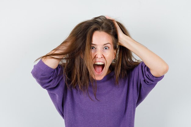 Young female holding hands on hair in woolen shirt and looking crazy , front view.