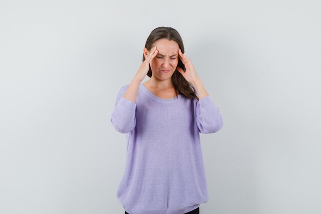 Young female holding hands on head in lilac blouse and looking stressful. front view.