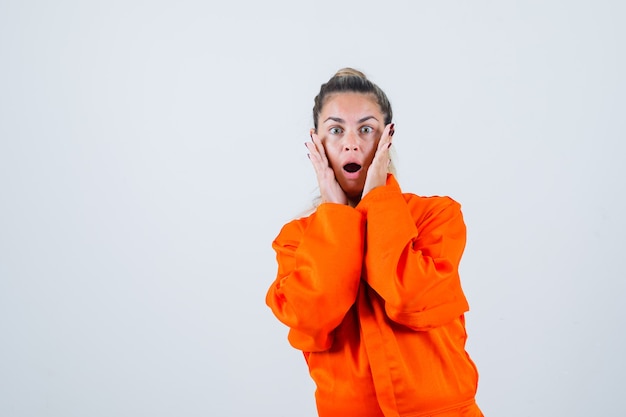 Young female holding hands on her face in worker uniform and looking astonished. front view.