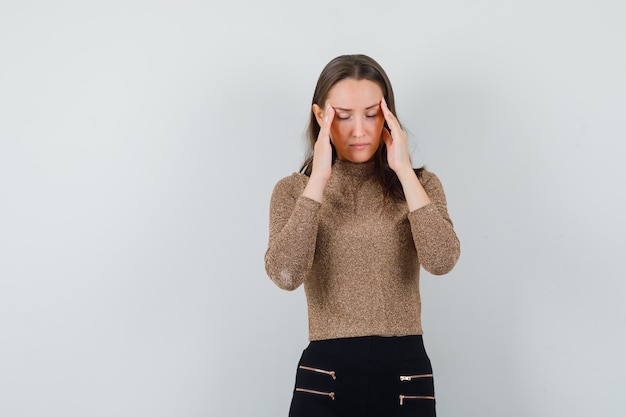 Young female holding hands on her temples in blouse,skirt and looking stressful , front view. space for text