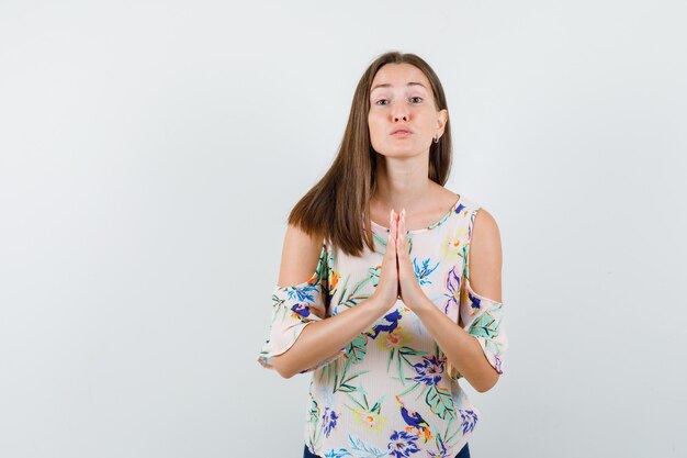 Young female holding hands in praying gesture in shirt, front view.