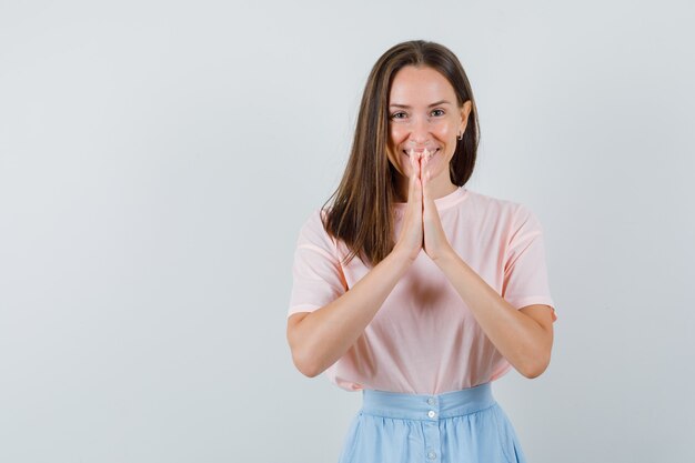 Молодая женщина, взявшись за руки в молитвенном жесте в футболке, юбке и выглядя позитивно. передний план.