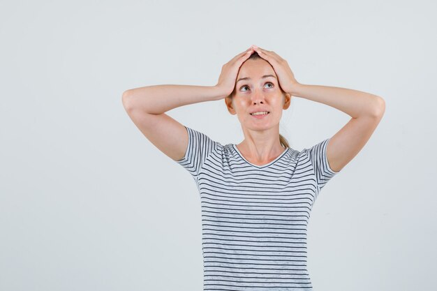 Young female holding head with hands in striped t-shirt and looking confused. front view.