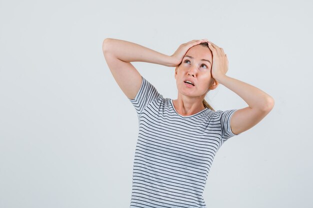 Young female holding head with hands in striped t-shirt and looking worried. front view.