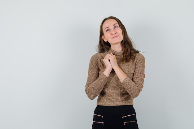 Young female holding her combined hands on her chest in golden blouse and looking hopeful. front view. space for text