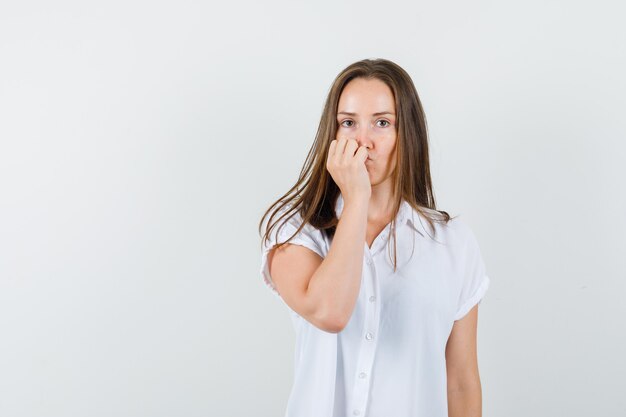 Young female holding her fist on her face in white blouse and looking upset.