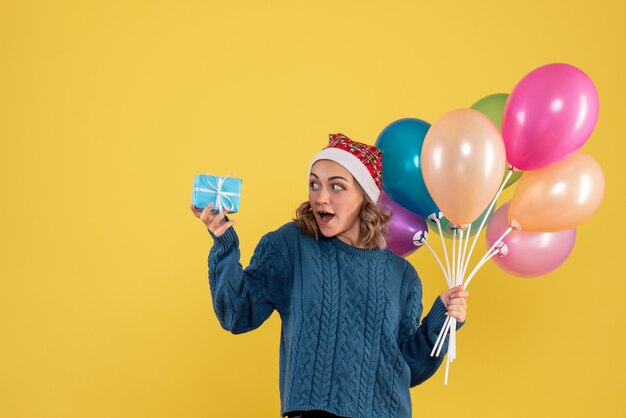 young female holding little present and balloons on yellow