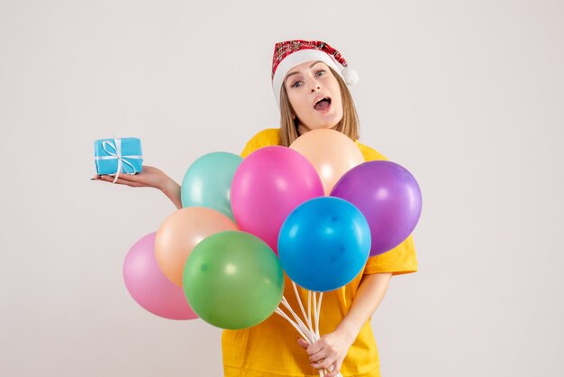 young female holding little present and colorful balloons on white